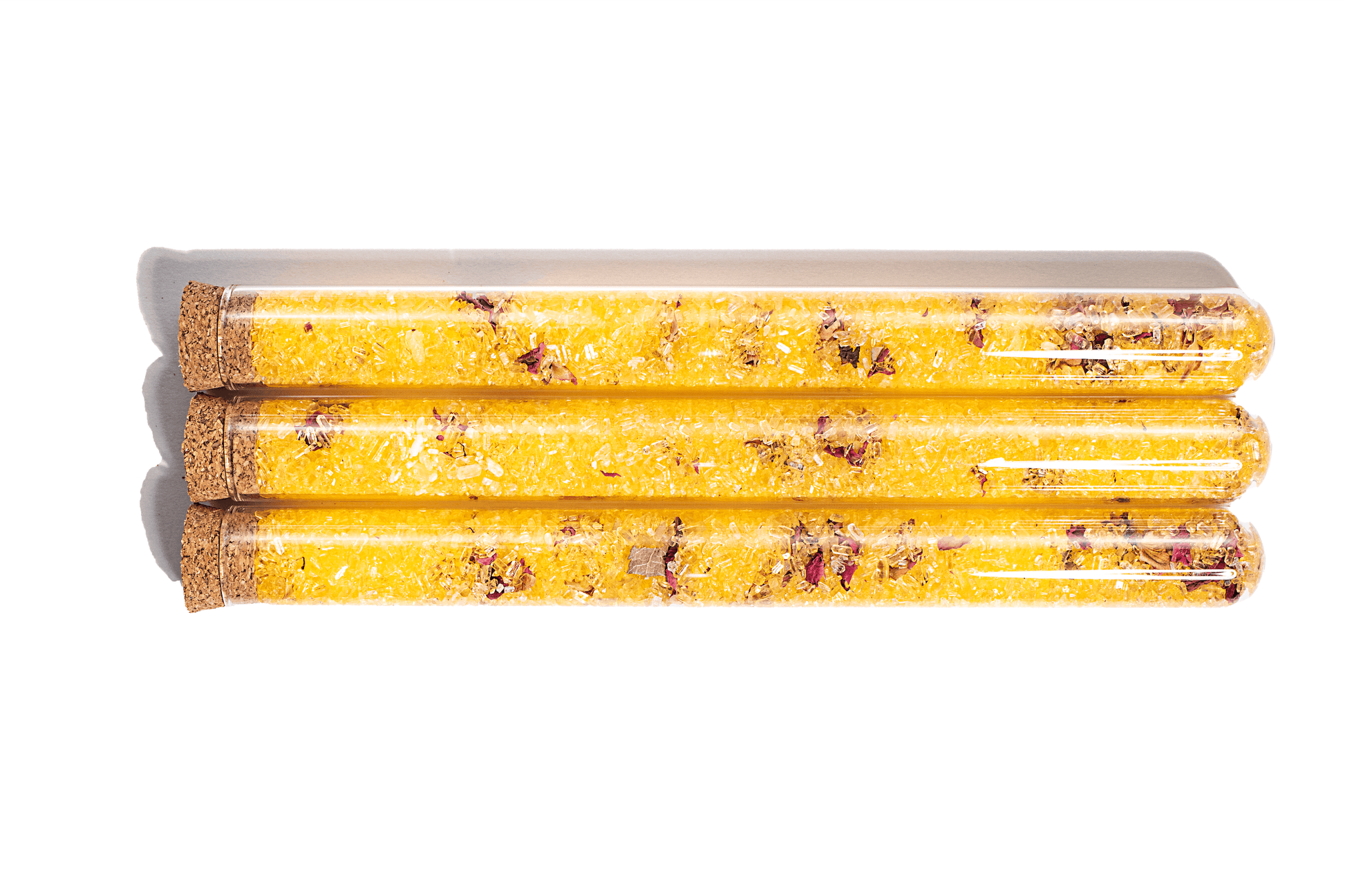 Image of 3 yellow bath salts in clear glass tubes with Rose Petals. The salts appear to have a fine, powdery texture and are a vibrant shade of yellow. Dried rose petals are visible inside the tubes, adding a decorative touch to the product. The tubes are arranged in a neat row against a white background.